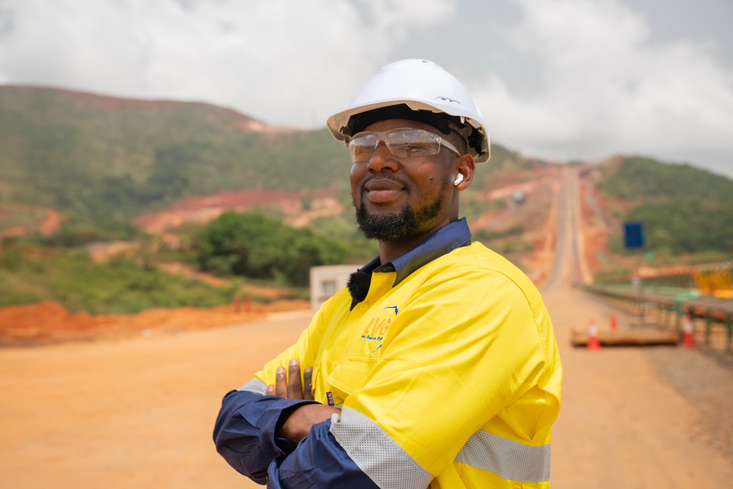 Ousmane, directeur général de LVG, portant un EPI haute visibilité, posant sur un site du projet Simandou avec les collines en arrière-plan.